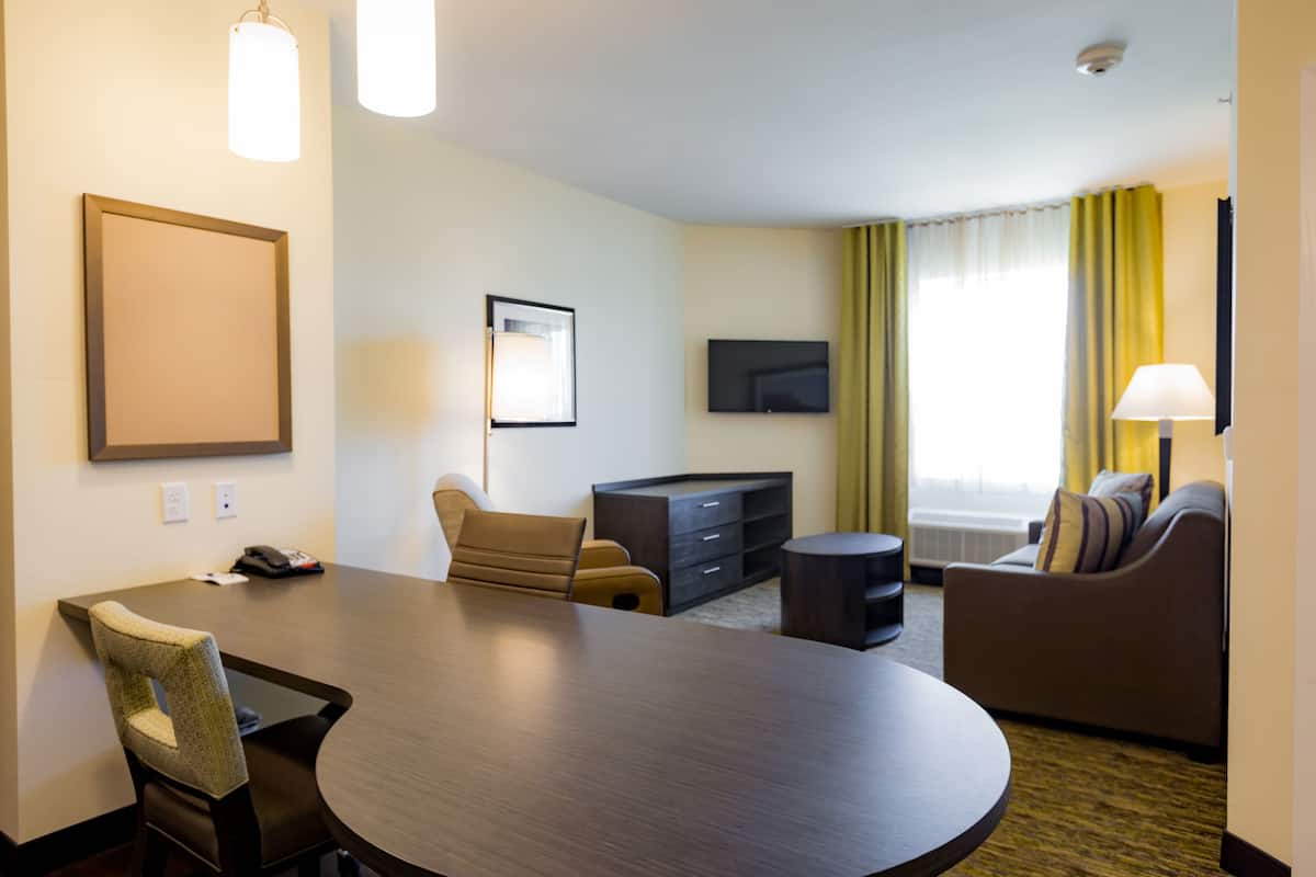 Una habitación de hotel con una mesa de comedor redonda, un sofá, un televisor y una lámpara.