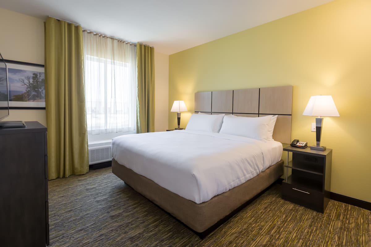 Habitación de hotel con una cama grande, dos mesitas de noche con lámparas, un escritorio con teléfono y una ventana con cortinas.