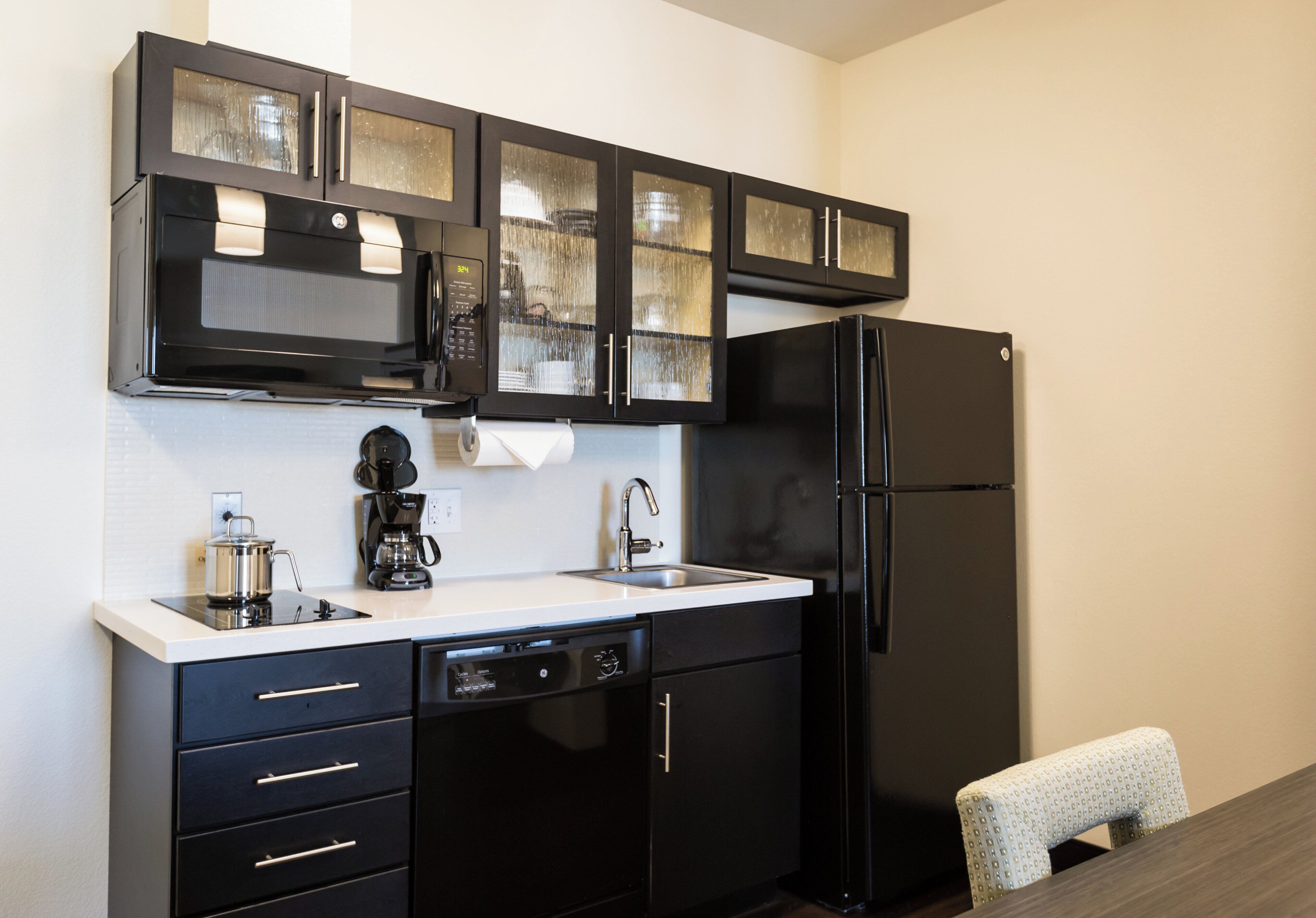 A compact kitchen with a microwave, coffee maker, dishwasher, and a black refrigerator.