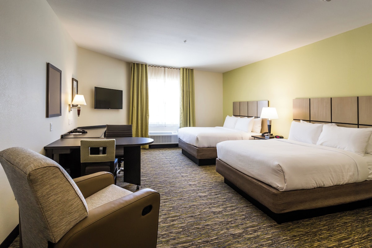 A hotel room with two beds, a desk, a chair, a TV, and a window with curtains.
