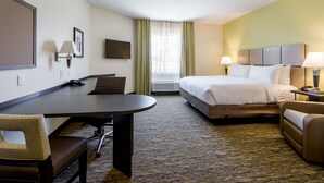 Habitación de hotel con cama, escritorio, silla, televisor y ventana con cortinas.