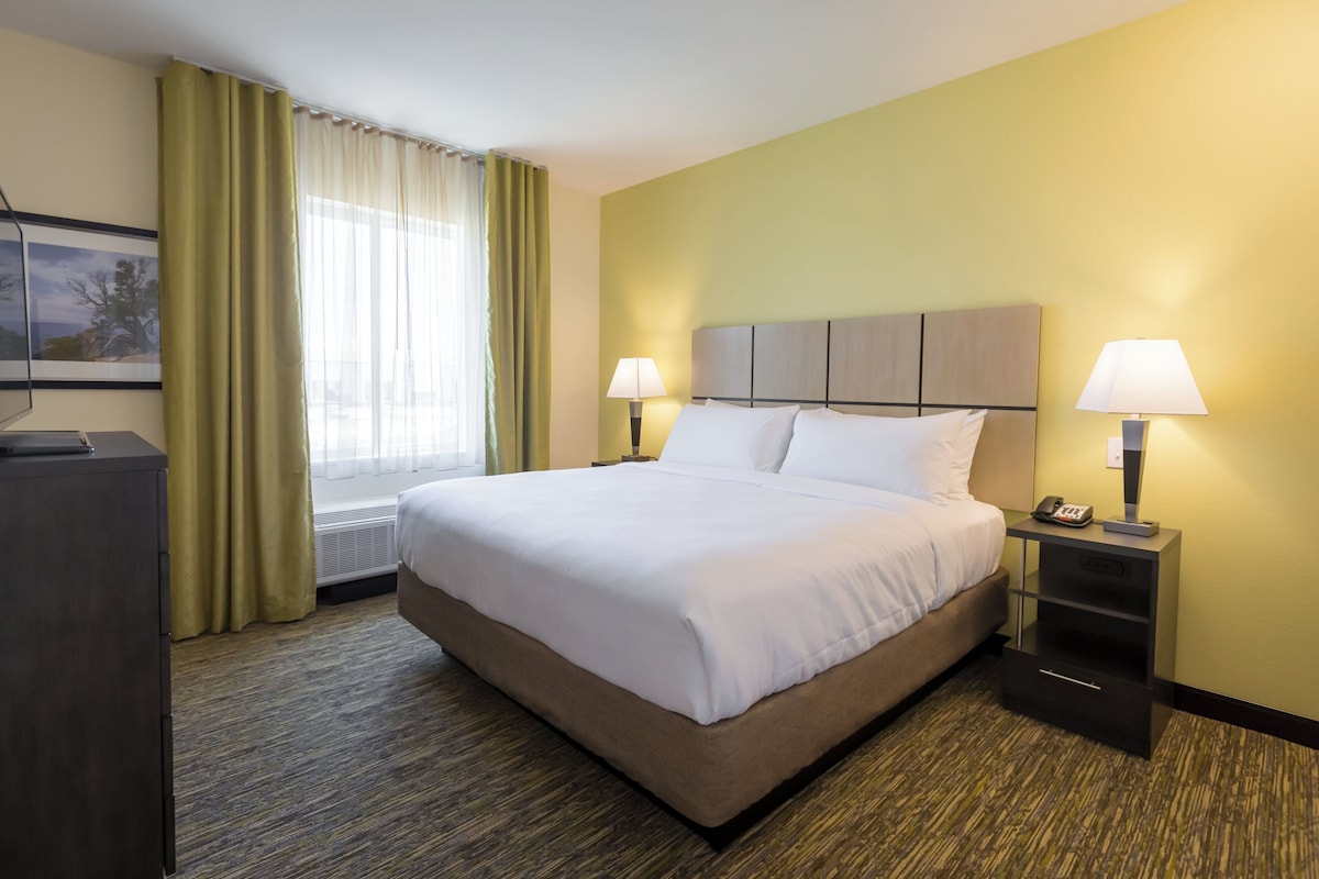 A hotel room with a large bed, two bedside tables with lamps, a desk, and a window with curtains.