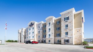 Un hôtel à plusieurs étages, doté d’une façade en pierre, de nombreuses fenêtres et d’un parking rempli de voitures.