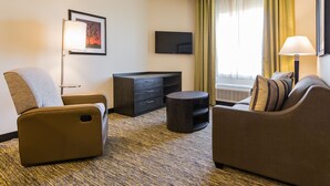 Habitación de hotel con sofá, una silla, televisor, escritorio y lámpara.