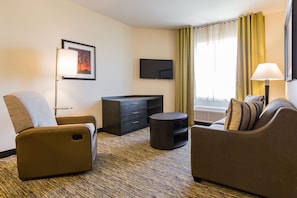 A hotel room with a sofa, a chair, a TV, a desk, and a lamp.
