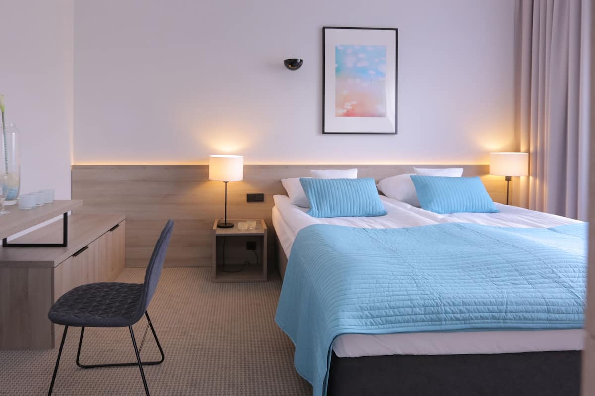 Ein Hotelzimmer mit einem Bett, Nachttischlampen, einem Schreibtisch mit Stuhl und einem kleinen Tisch mit Gläsern.
