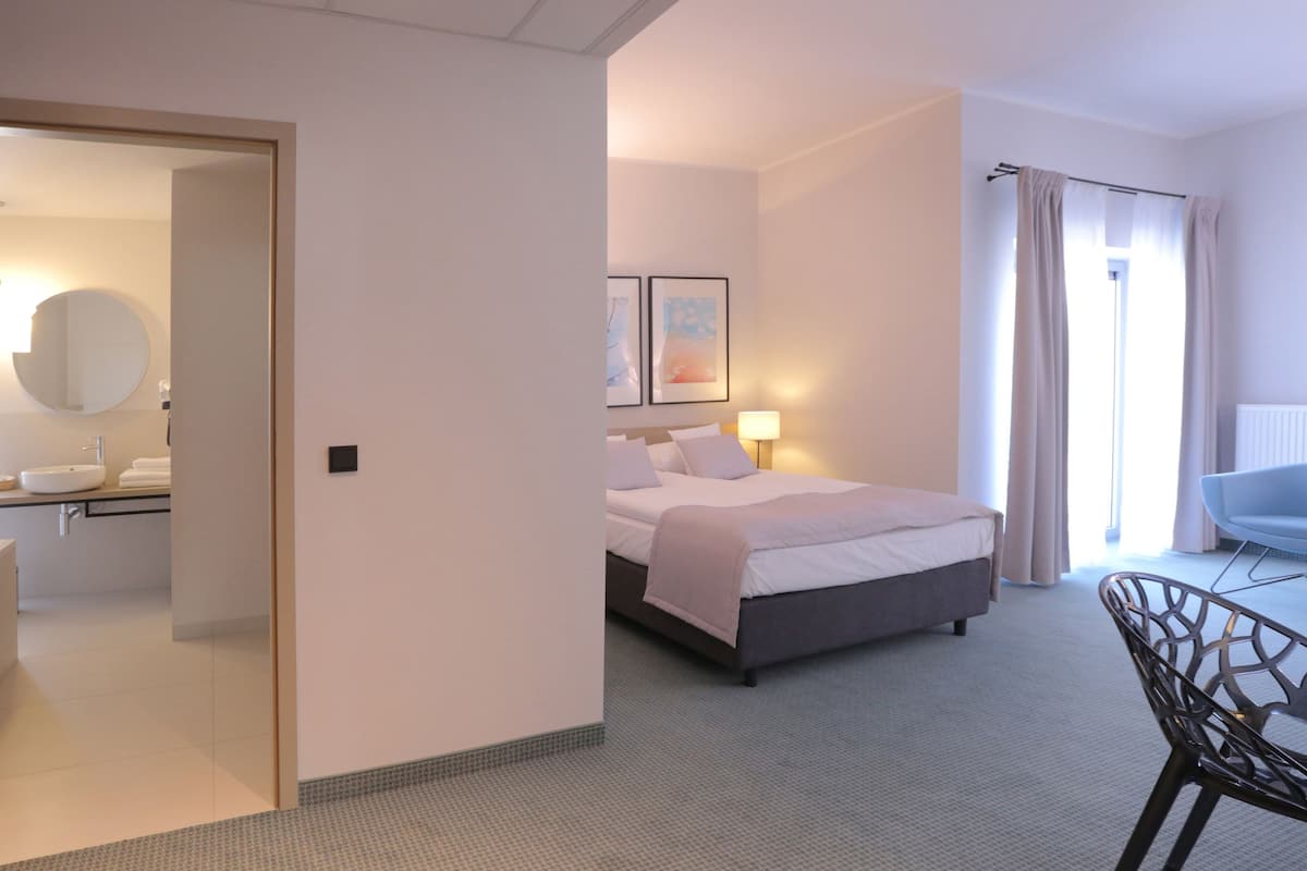Ein Hotelzimmer mit Bett, Schreibtisch, Stuhl, Badezimmer mit Waschbecken und Spiegel sowie einem Fenster mit Vorhängen.