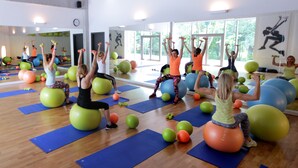 Een fitnessles waarbij deelnemers oefeningen doen met ballen en gewichten in een ruime, goed verlichte ruimte met grote ramen en spiegels.