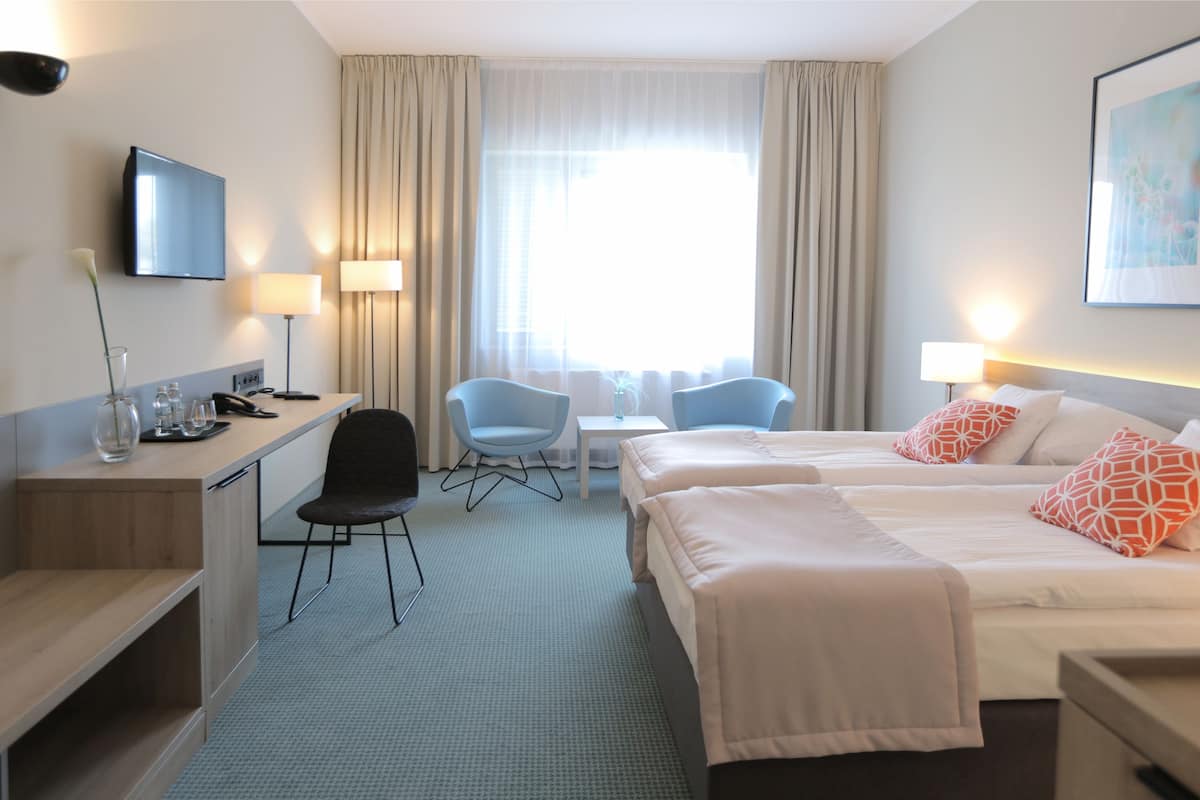 Ein Hotelzimmer mit zwei Betten, einem Schreibtisch, einem Stuhl, einem Fernseher und einem Fenster mit Vorhängen.