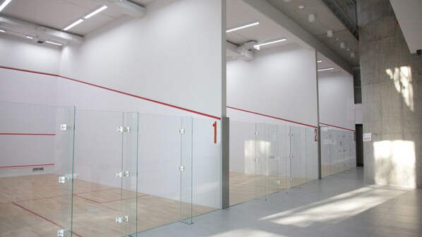 Una cancha de squash con paredes de vidrio, taquillas numeradas y piso de madera.