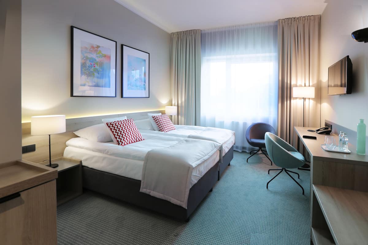 Ein Hotelzimmer mit einem großen Bett, einem Schreibtisch, einem Stuhl, einem Fernseher und zwei gerahmten Bildern an der Wand.