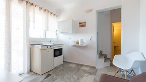 A compact kitchen with a microwave, oven, and sink, a white chair, and a staircase leading to a bathroom. - Poseidon Apartments (Kefalonia)