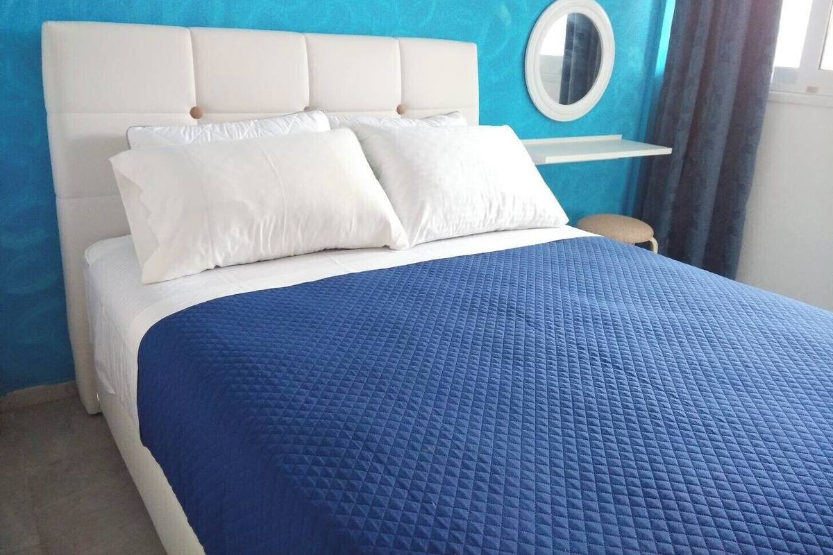 A bed with a white headboard, two white pillows, and a blue quilted bedspread.