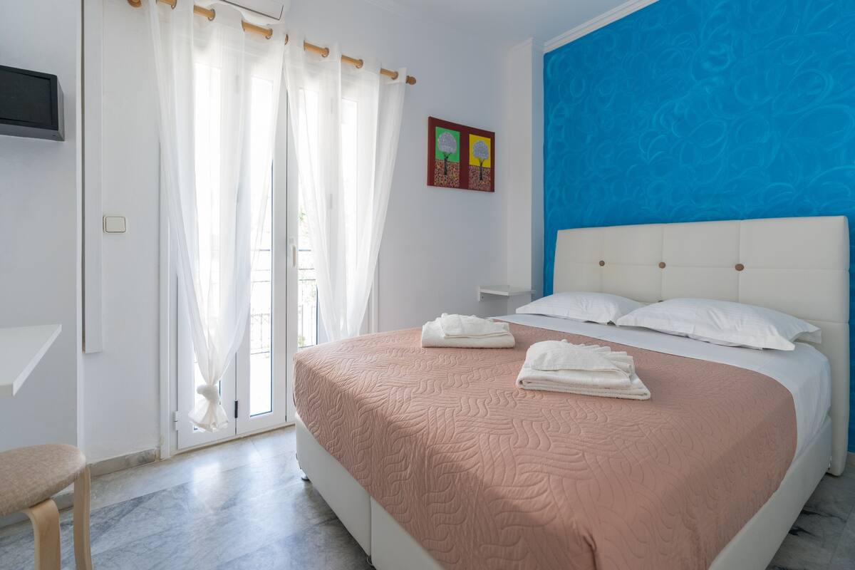 A bedroom with a bed, a bench, a TV, and a door with curtains.