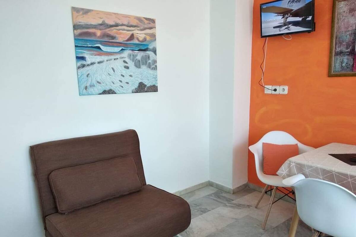 A room with a brown sofa, a TV mounted on the wall, and a table with two chairs.