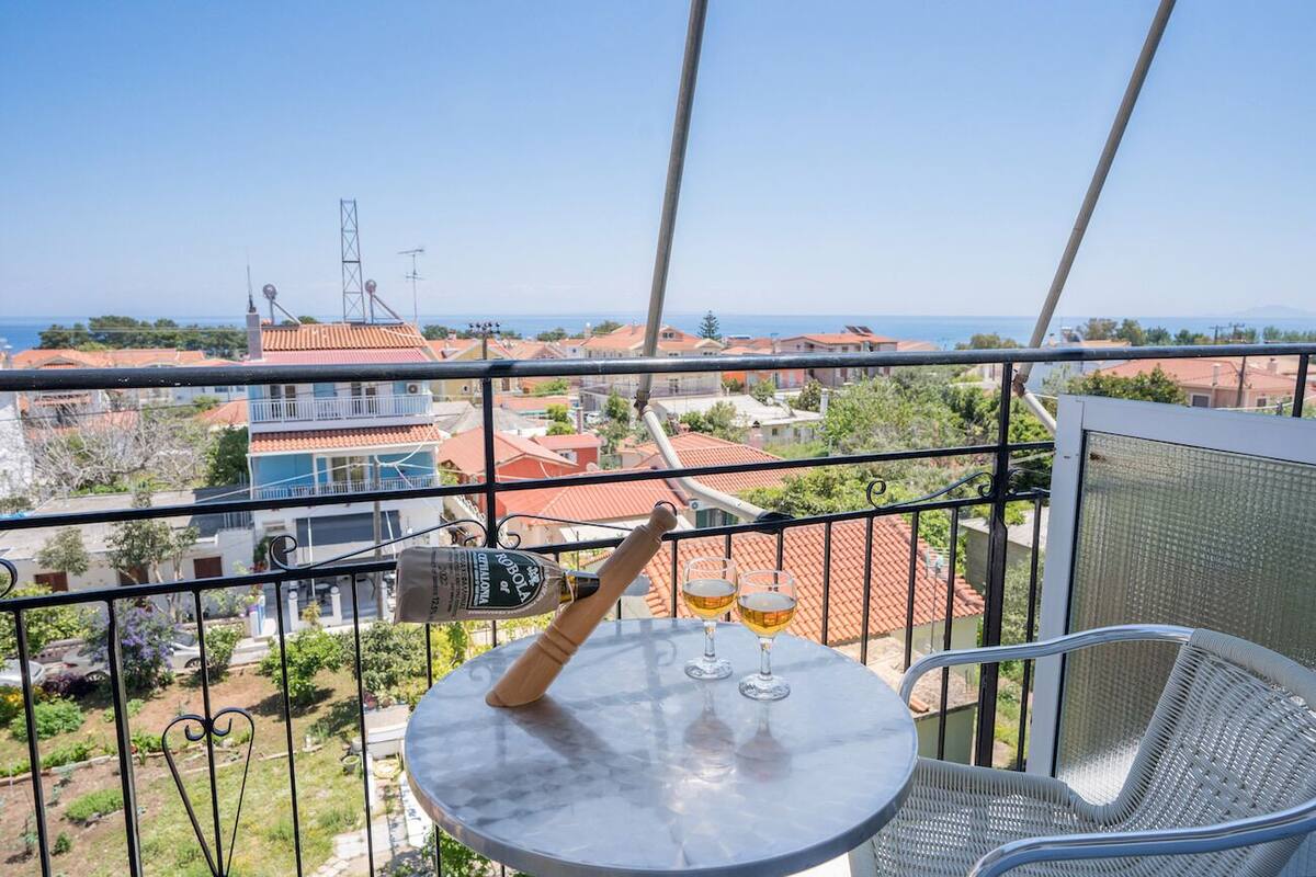 A balcony with a table, two glasses, and a bottle of alcohol.