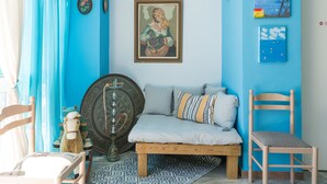 A room with a blue wall, a wooden bench, a chair, a sofa, a decorative wall hanging, and a wall-mounted lamp. - Poseidon Apartments (Kefalonia)