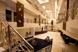 Un amplio vestíbulo de hotel con una zona de estar central, una escalera y un mostrador de recepción.