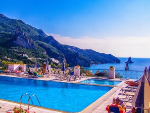 Área de piscina com espreguiçadeiras e guarda-sóis, com vista para a costa montanhosa.