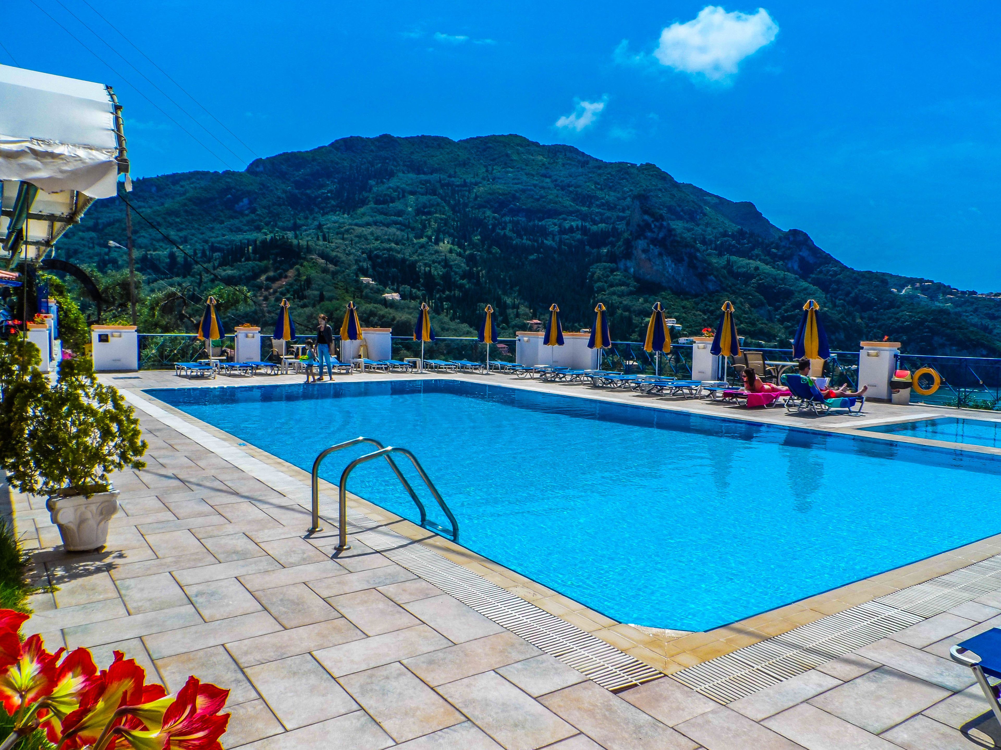 Ein Schwimmbecken mit Liegestühlen und Sonnenschirmen, umgeben von einer gebirgigen Landschaft.