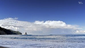 Une plage avec des vagues, un phare au loin et un ciel dégagé.