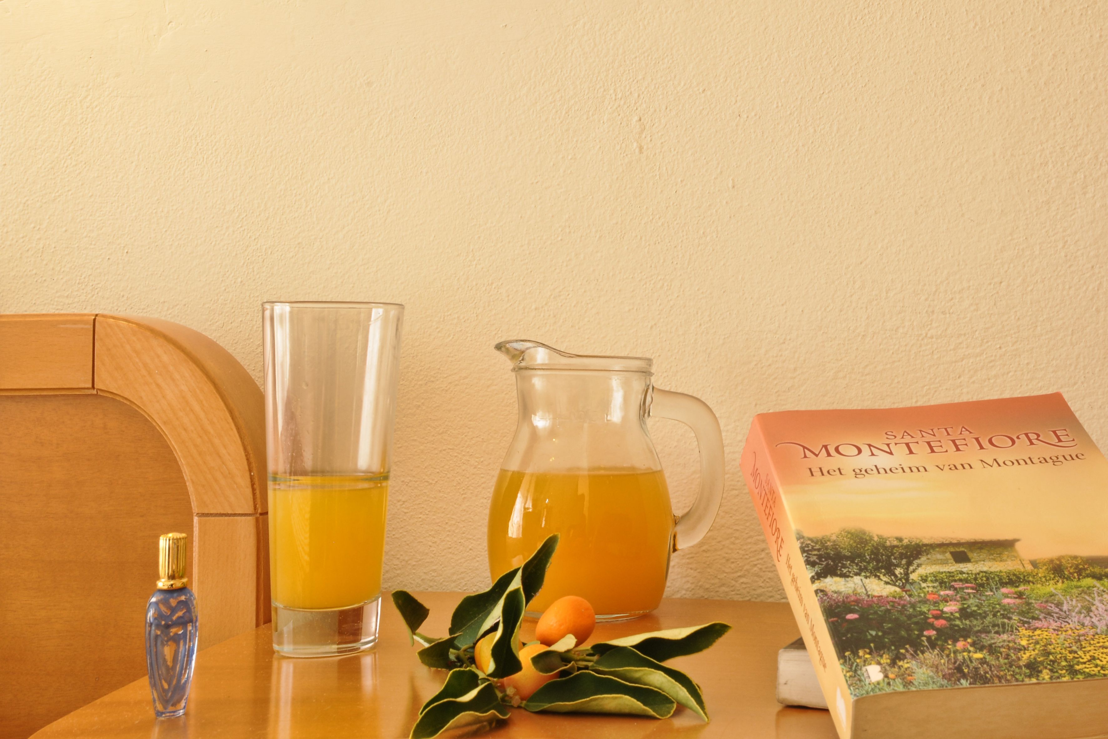 A table with a book, a pitcher of orange juice, and a glass of orange juice.