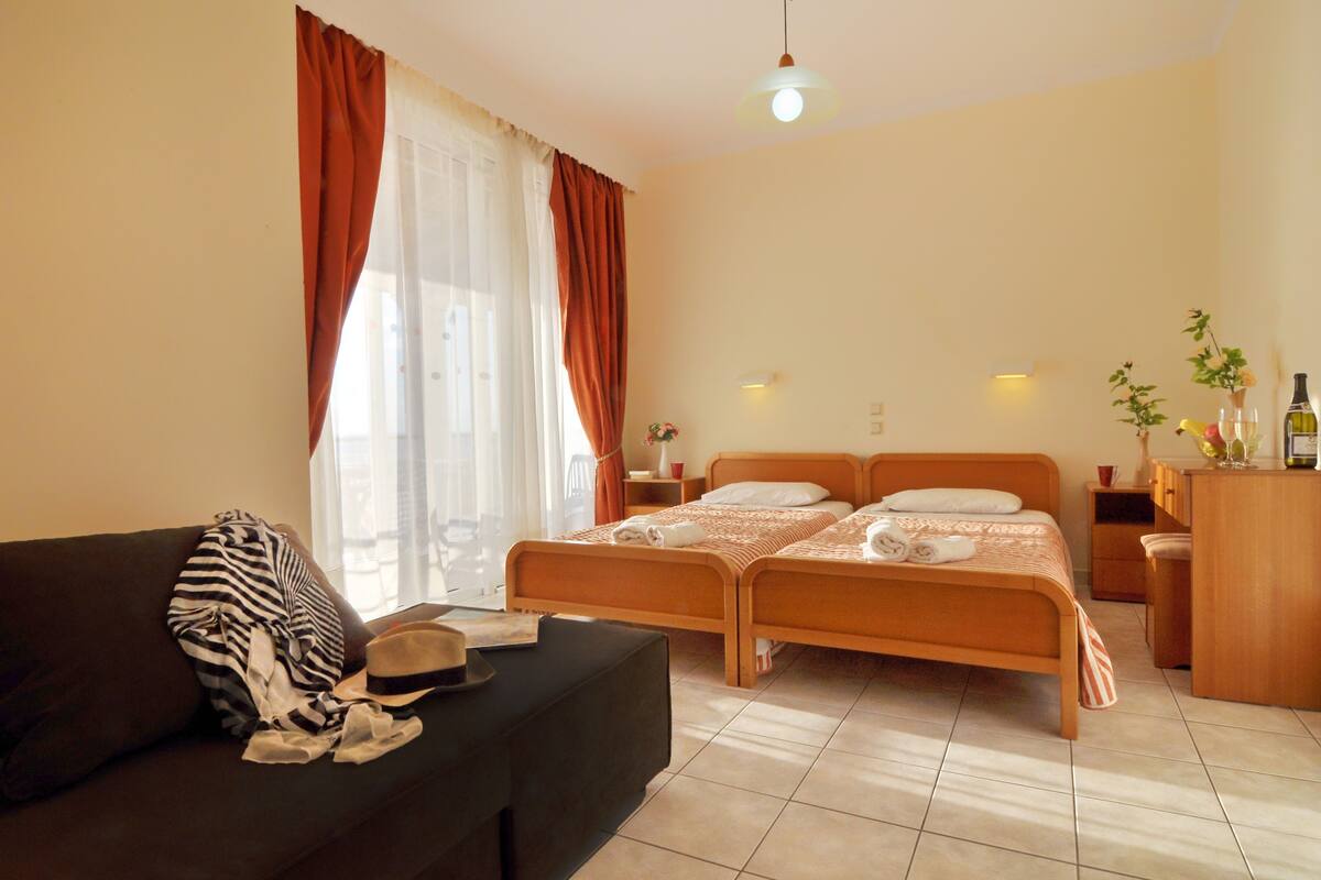 Une chambre d’hôtel avec un lit, un canapé, un bureau et une fenêtre avec des rideaux.