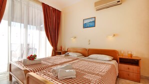 Une chambre d’hôtel avec deux lits, une table de chevet avec une lampe, un tableau au mur et un appareil de climatisation.