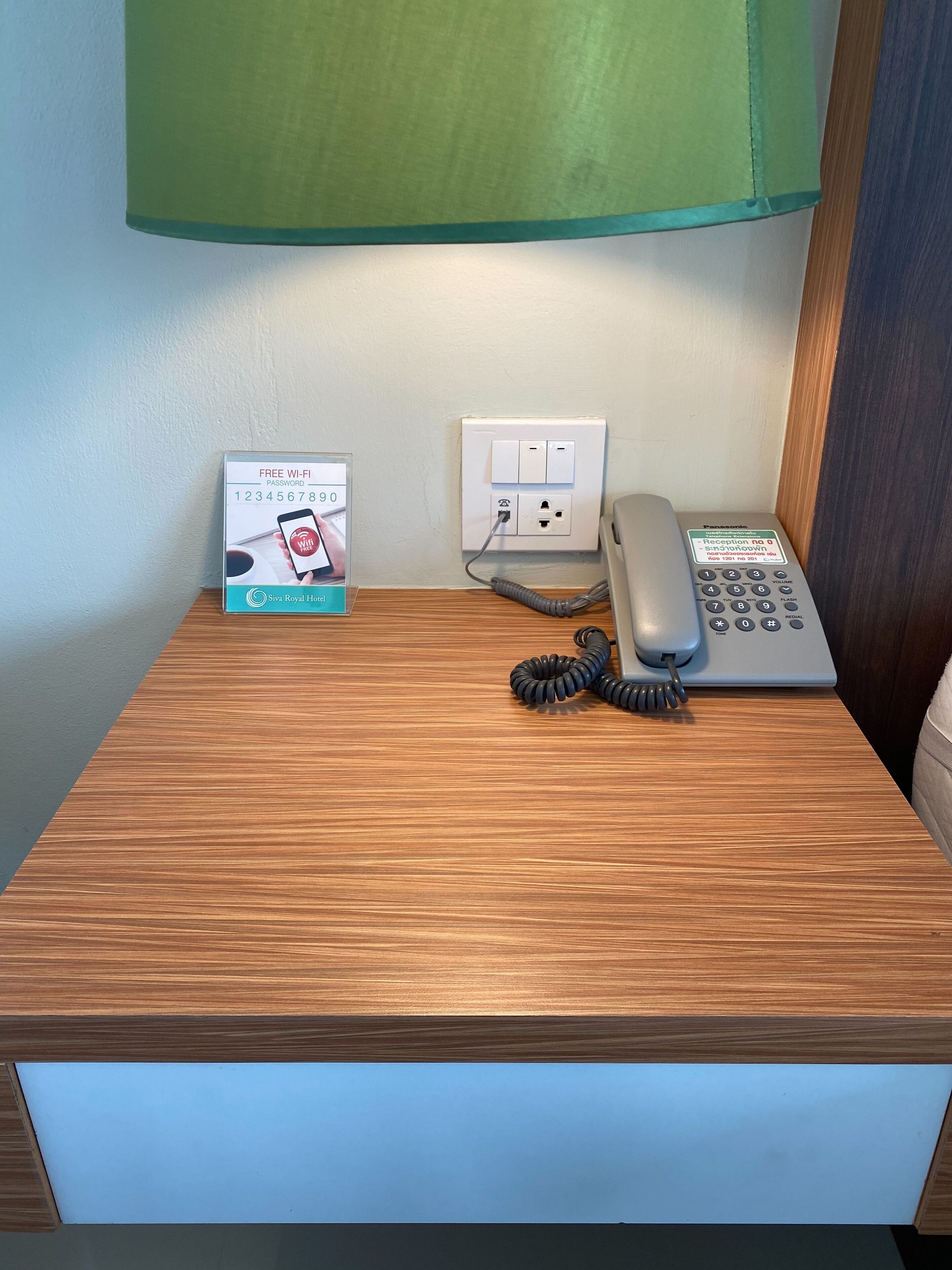 Escritorio de madera con un teléfono, un cable de extensión enrollado y un cartel que indica la contraseña de Wi-Fi gratuita.