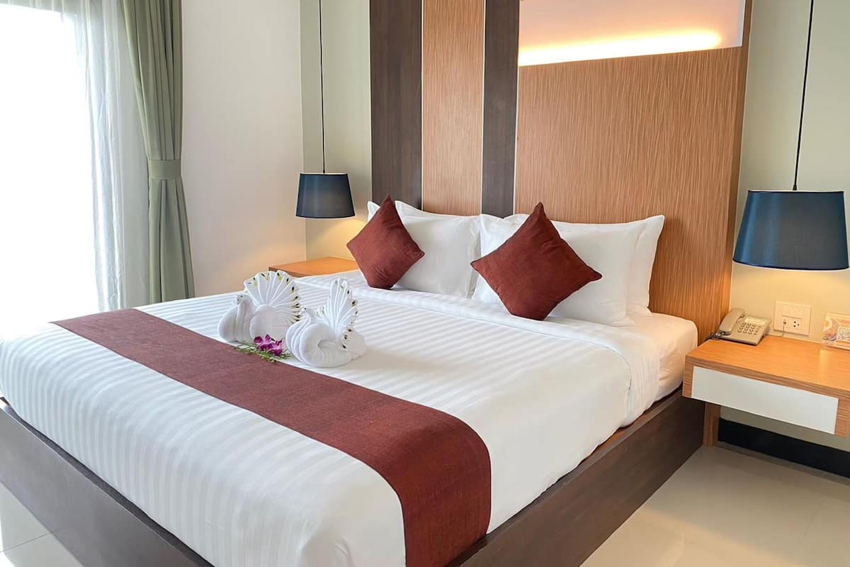 Una habitación de hotel con una cama grande, dos mesitas de noche, una lámpara y un teléfono.