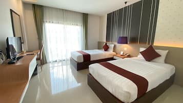 A hotel room with two beds, a desk with a computer, a TV, and a large window with curtains.