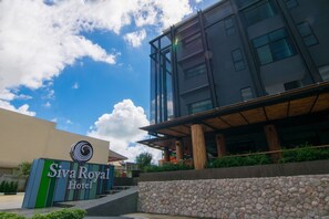 The exterior of Siva Royal Hotel with a modern architectural design, a stone wall in front, and a clear blue sky with clouds. - Siva Royal Hotel (Phatthalung)