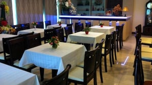 Un restaurant doté de nombreuses tables et chaises, d’un bar et agrémenté de fleurs décoratives.