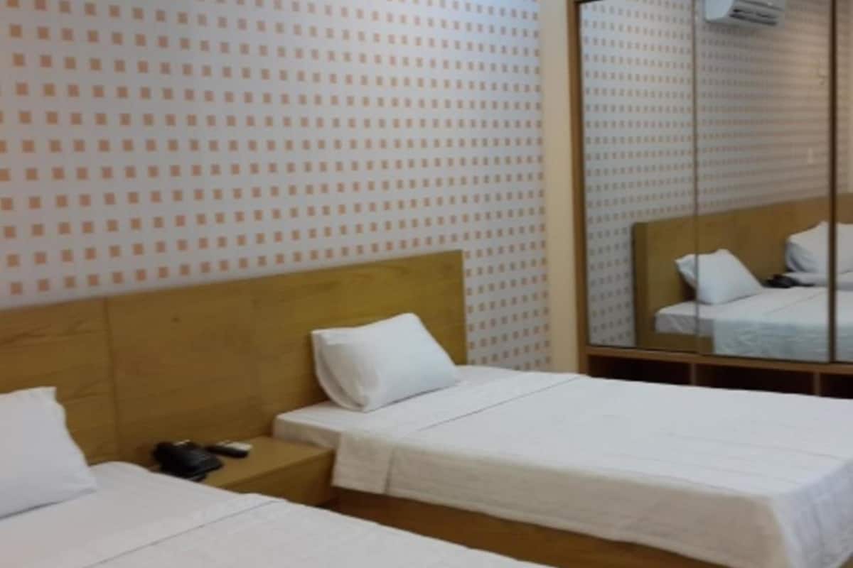 Ein Hotelzimmer mit zwei Betten, einem Holzkopfende, einem kleinen Nachttisch mit Telefon und einem Spiegel an der Wand.