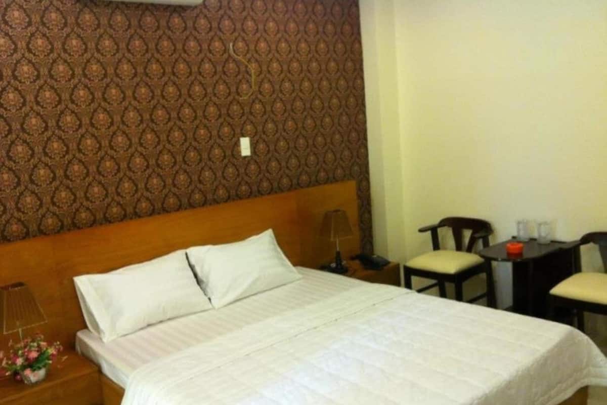 Ein Hotelzimmer mit einem großen Bett, einem Nachttisch mit Lampe, einem Sessel und einem kleinen Tisch mit einem roten Gegenstand darauf.