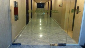 Un couloir d’hôtel doté d’un sol en marbre, de portes en verre et d’un plafond pourvu d’un éclairage encastré.