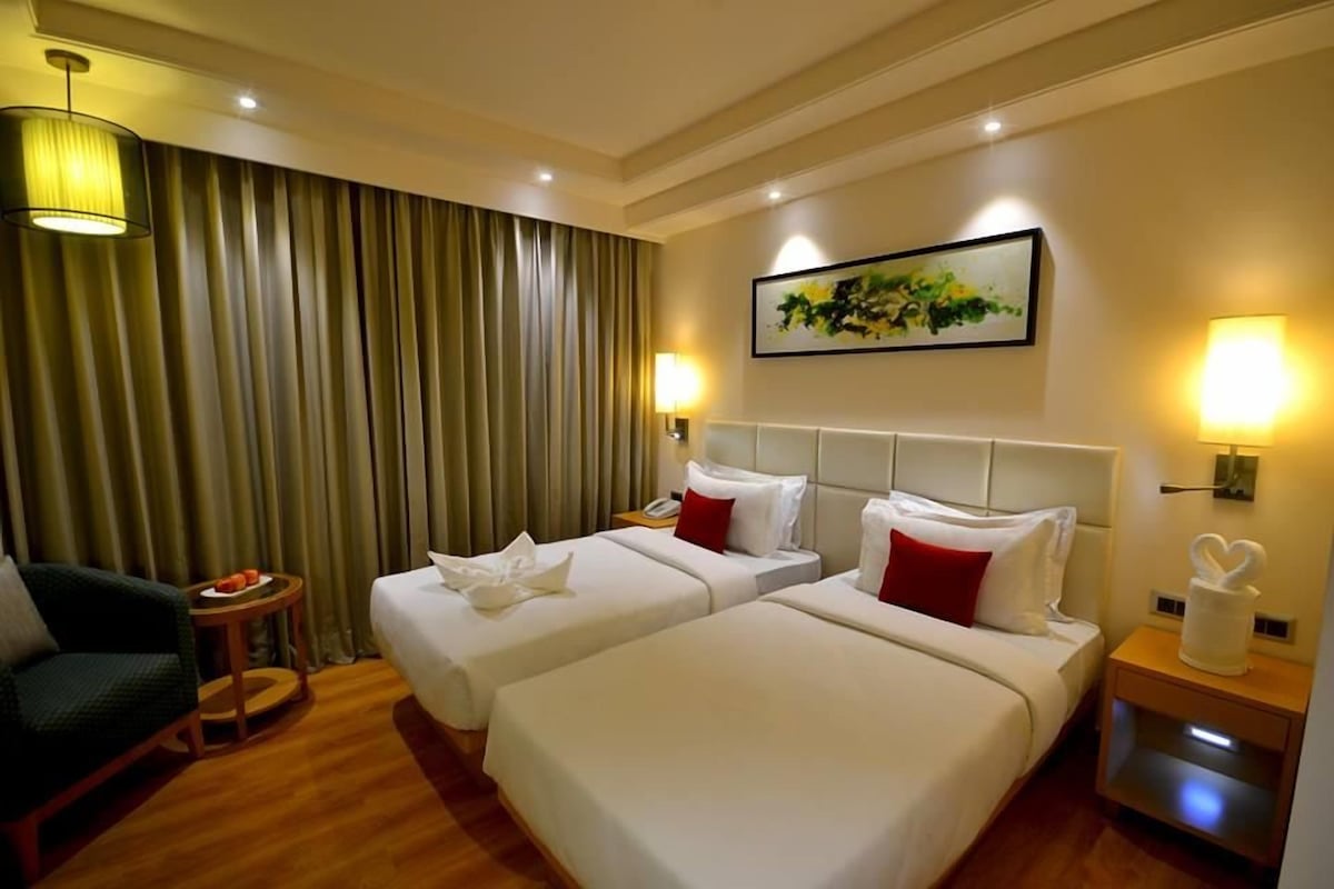 Une chambre d’hôtel avec deux lits, une chaise, une petite table avec des fruits et un tableau au mur.