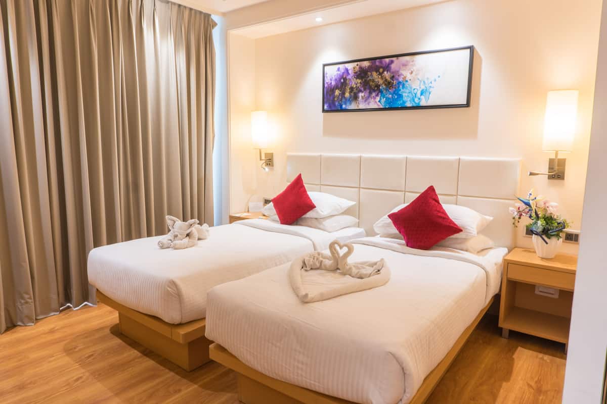A hotel room with two beds, each with a red pillow and a towel. There is a painting on the wall and a nightstand with a lamp and a vase of flowers.