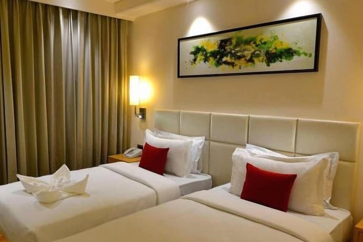 Une chambre d’hôtel avec deux lits, une tête de lit, des lampes de chevet, un tableau et un objet décoratif sur la table de chevet.