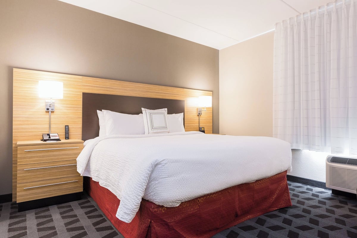 Une chambre d’hôtel avec un grand lit, une tête de lit en bois, deux tables de chevet avec des lampes, un mur d’accent rouge et une moquette à motifs.