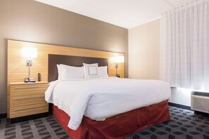 A hotel room with a large bed, a wooden headboard, two bedside tables with lamps, a red accent wall, and a patterned carpet.