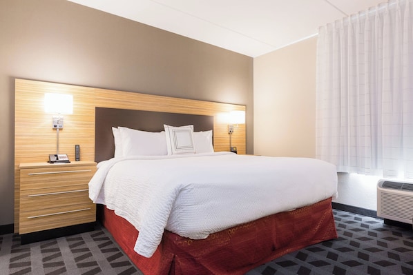 Habitación de hotel con una cama grande, un cabecero de madera, dos mesitas de noche con lámparas, una pared de acento roja y una alfombra estampada.
