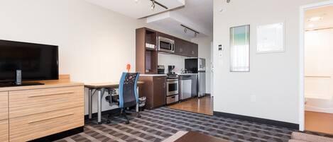 Una cocina moderna con electrodomésticos de acero inoxidable, un comedor con una mesa y sillas de madera, y un televisor sobre un mueble de madera.