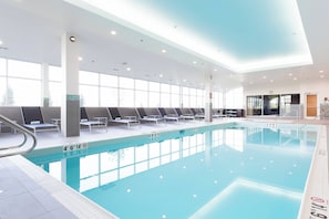 Una piscina interior con agua cristalina, tumbonas y un diseño moderno de techo.