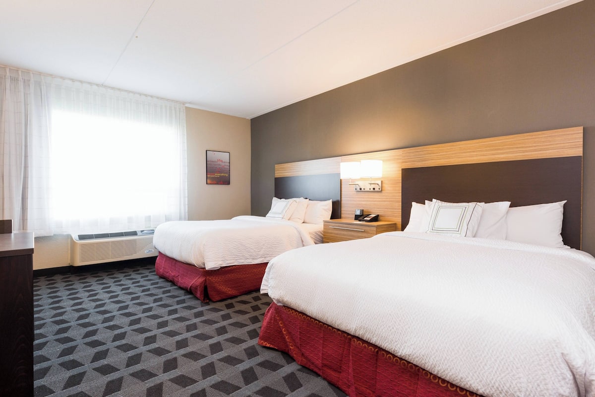 Une chambre d’hôtel avec deux lits, un bureau et une fenêtre avec des rideaux.