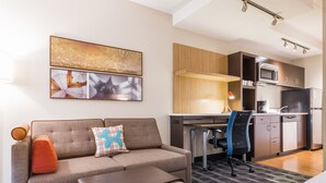Una habitación de hotel moderna con sofá, reposapiés, escritorio y kitchenette.