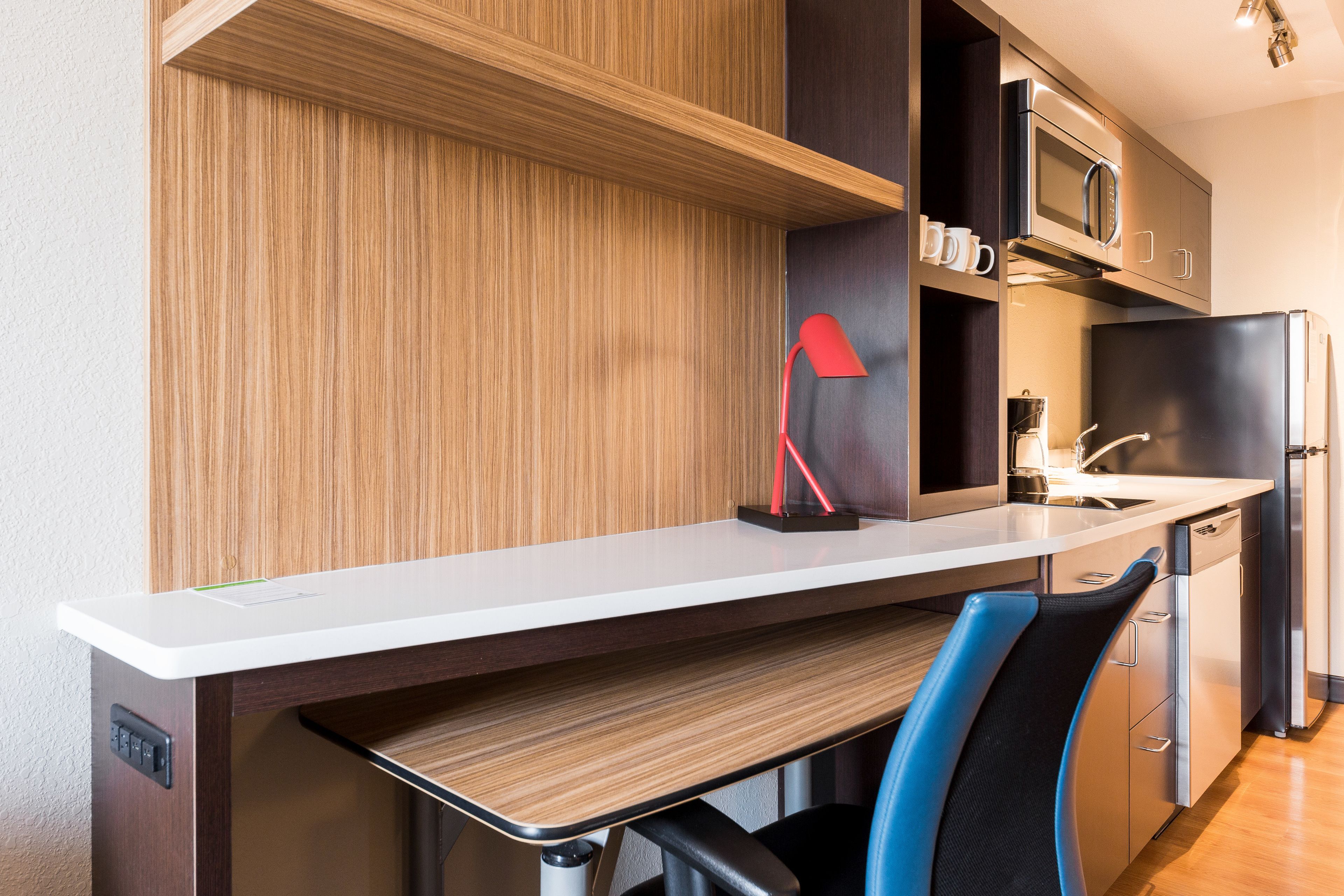 Una cocina moderna con armarios de madera, encimera blanca, lámpara roja, microondas, refrigerador y pileta.