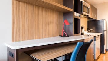 Una cocina moderna con armarios de madera, encimera blanca, lámpara roja, microondas, refrigerador y pileta.