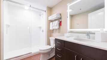 Un baño moderno con ducha acristalada, inodoro blanco, tocador con espejo y toallas ordenadas en un perchero.