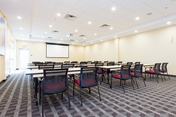 Un salón de conferencias con una mesa larga, sillas, una pantalla de proyector y piso alfombrado.